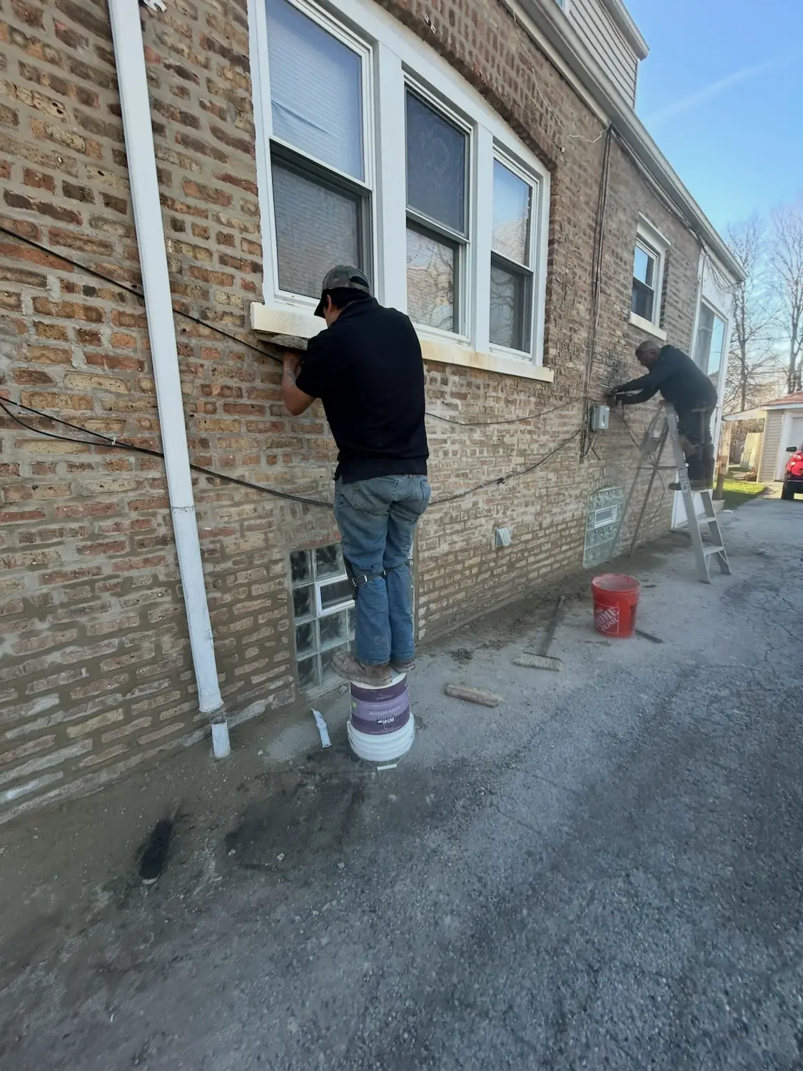 Two masons repairing brick beneath the windows of a Roseland home