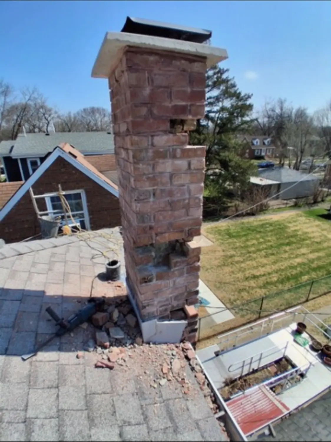 Chimney stack with failed brick removed and rubble on the shingle roof below