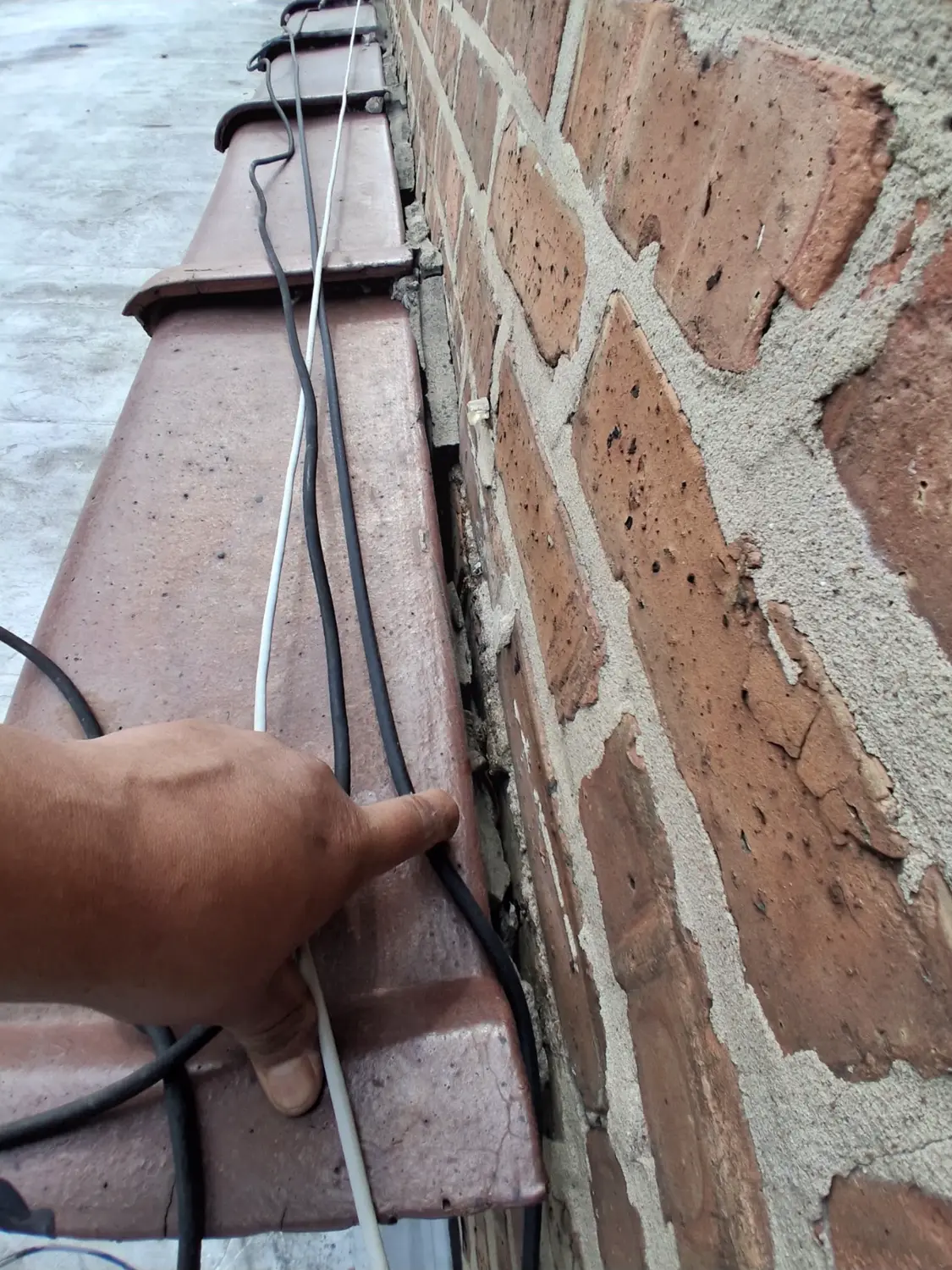 A gloved hand indicating the open joint between coping stone and parapet wall