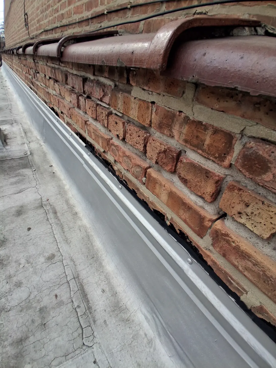 Deteriorated parapet brick and mortar below cracked coping stones