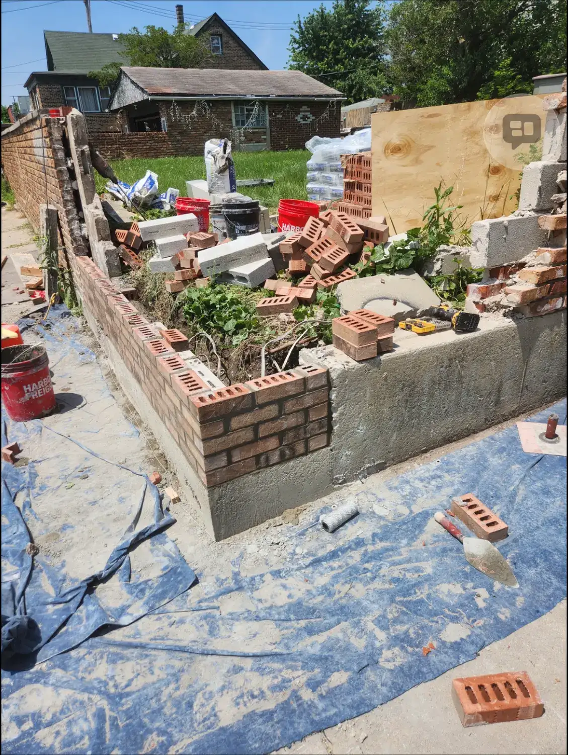 Boundary wall part demolished, with broken brick and block stacked on the tarpaulin